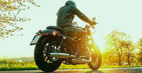Homem de costas andando de moto com cenário de por do sol ao fundo