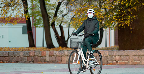 Foto de mulher andando de bicicleta utilizando capacete e máscara de proteção.