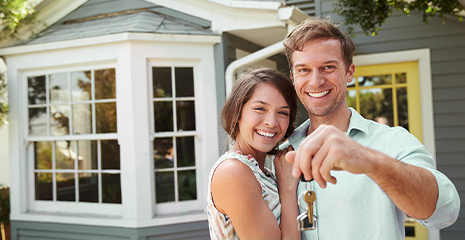 Casal feliz com chave na mão e casa nova de fundo