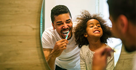 pai escovando o dente junto com a filha olhando para o espelho