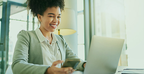 Mulher sorrindo olhando para um computador vestida em trajes sociais