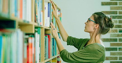 Imagem de mulher observando prateleira de livros enquanto seleciona um livro