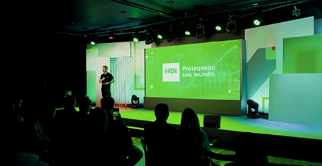 Foto de Eduardo dal Ri em um palco com o logotipo da HDI projetado atrás dele, em um telão