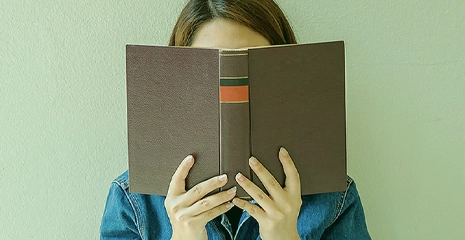 Mulher com o rosto escondido dentro do livro