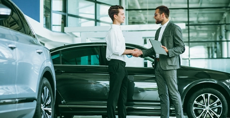 Homens se cumprimentando com carros ao fundo